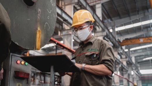 Factory worker with safety gear checks machinery, ensuring industrial safety compliance.